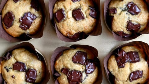Golden brown banana chocolate chip muffins in cupcake liners in a muffin tin.
