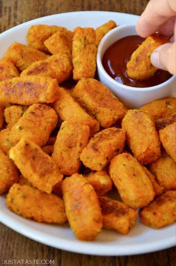 A plate of butternut squash tots and one being dipped in ketchup