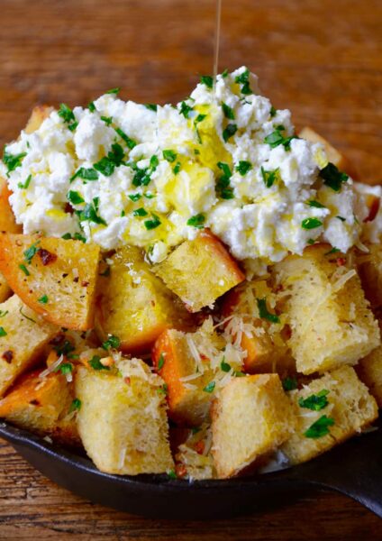 A skillet filled with cheesy garlic bread topped with ricotta cheese