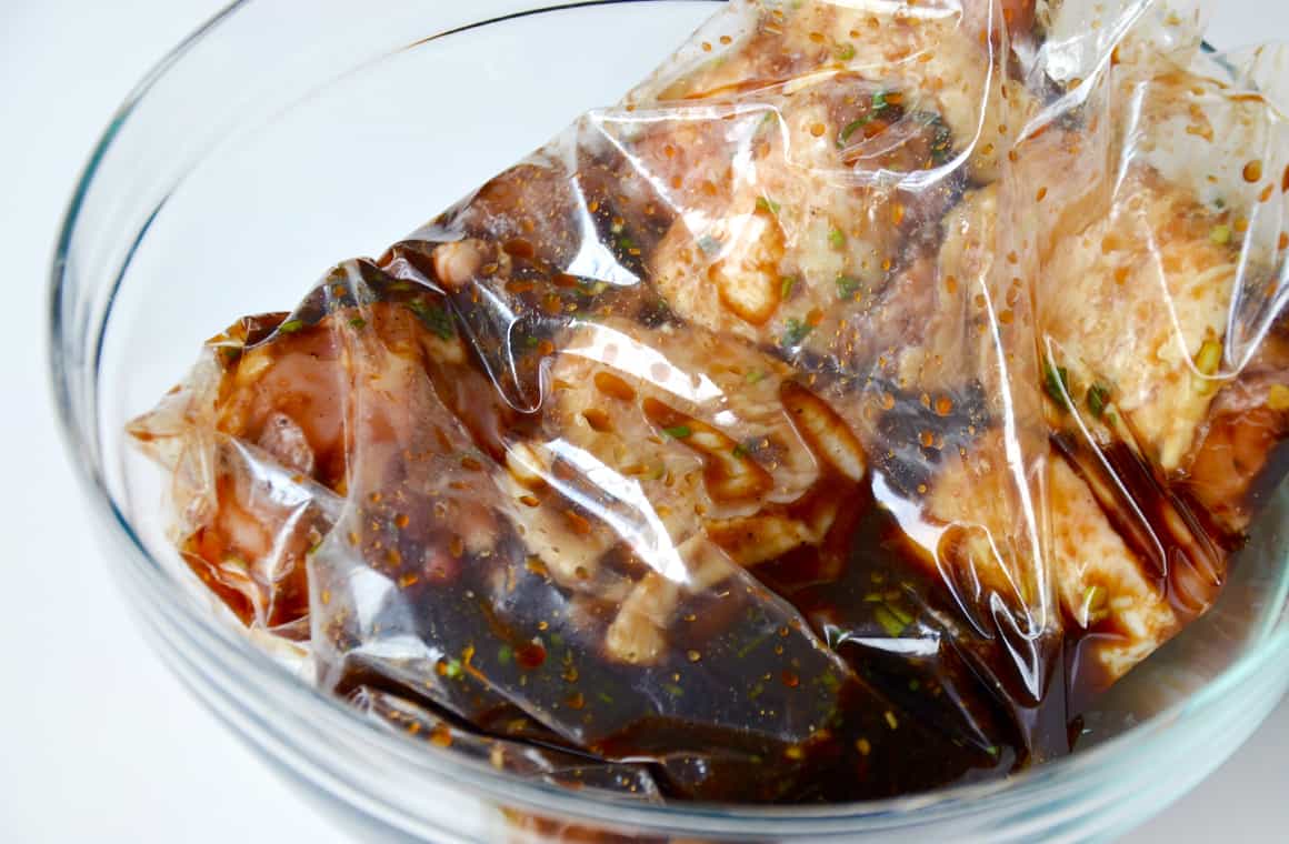 A clear bowl containing a plastic bag with marinating poultry