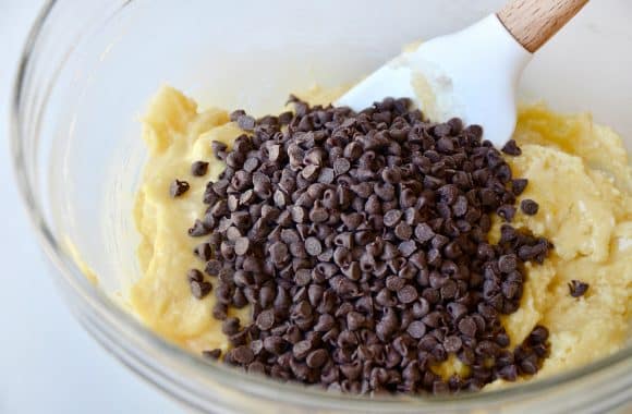 Mini chocolate chips in a glass bowl with cookie dough and a spatula