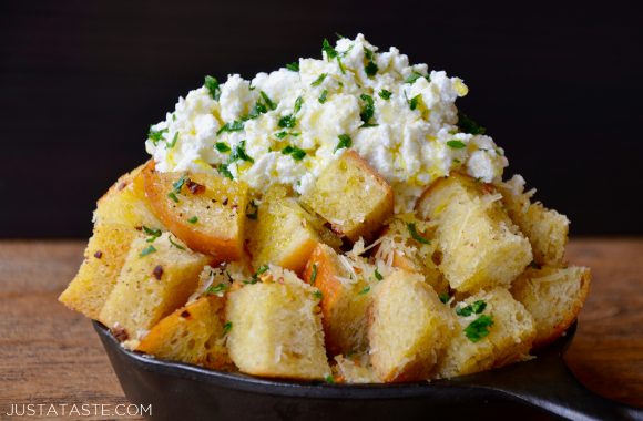 Cheesy garlic bread cubes in a skillet with ricotta cheese and herbs on top