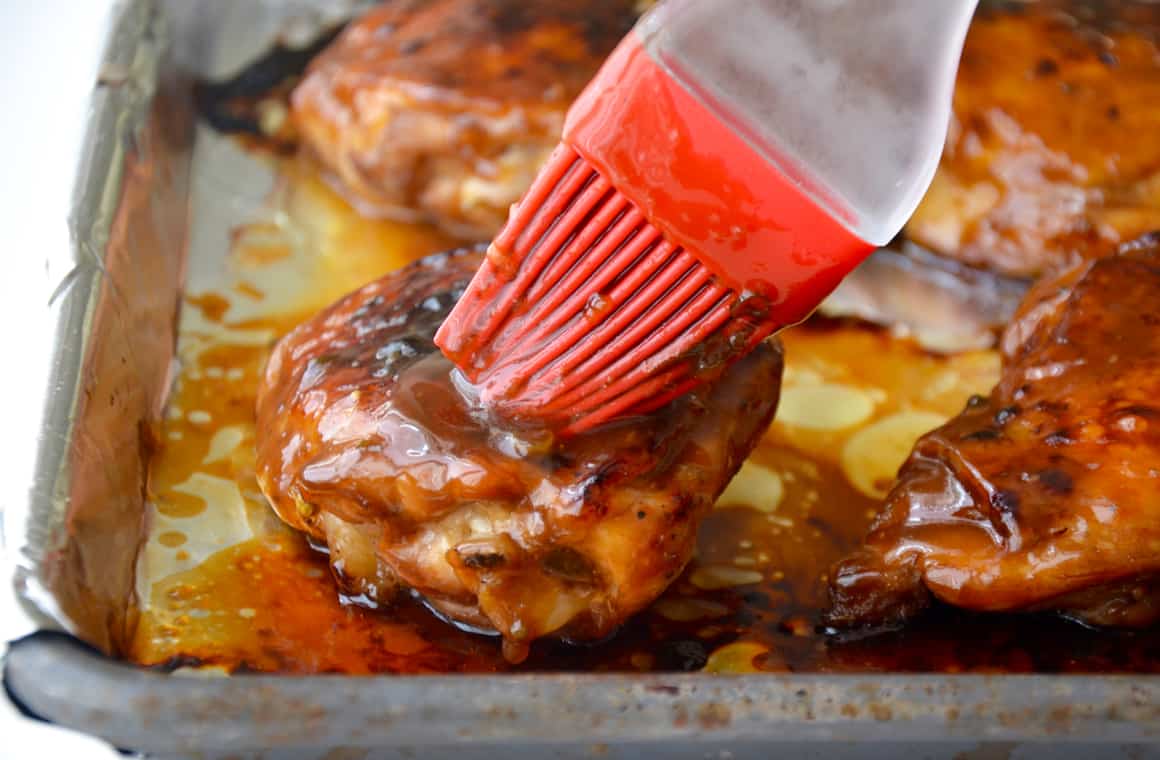 A food brush applies glaze atop baked chicken thighs