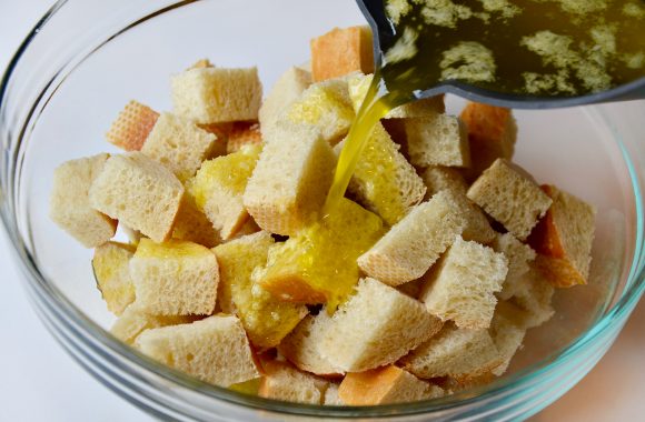 Cubes of bread in a glass bowl with garlic butter drizzled on top