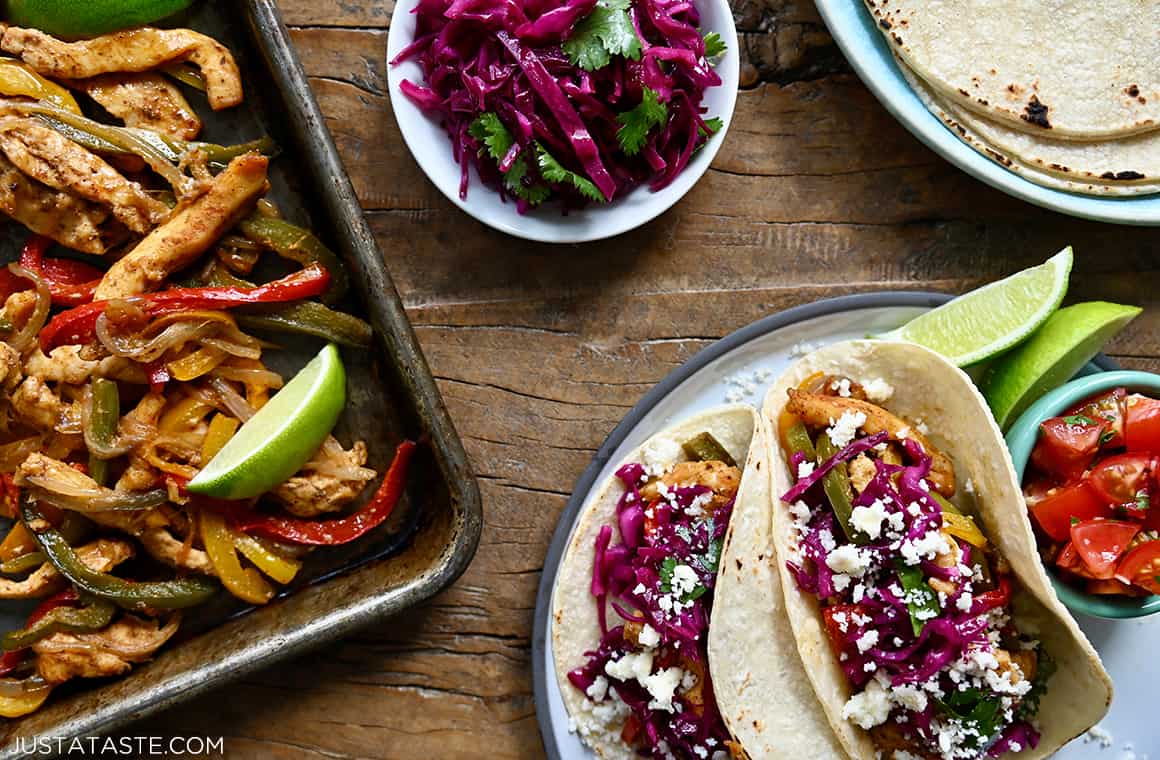 A top-down view of easy Sheet Pan Chicken Fajitas next to a plate of corn tortilla tacos