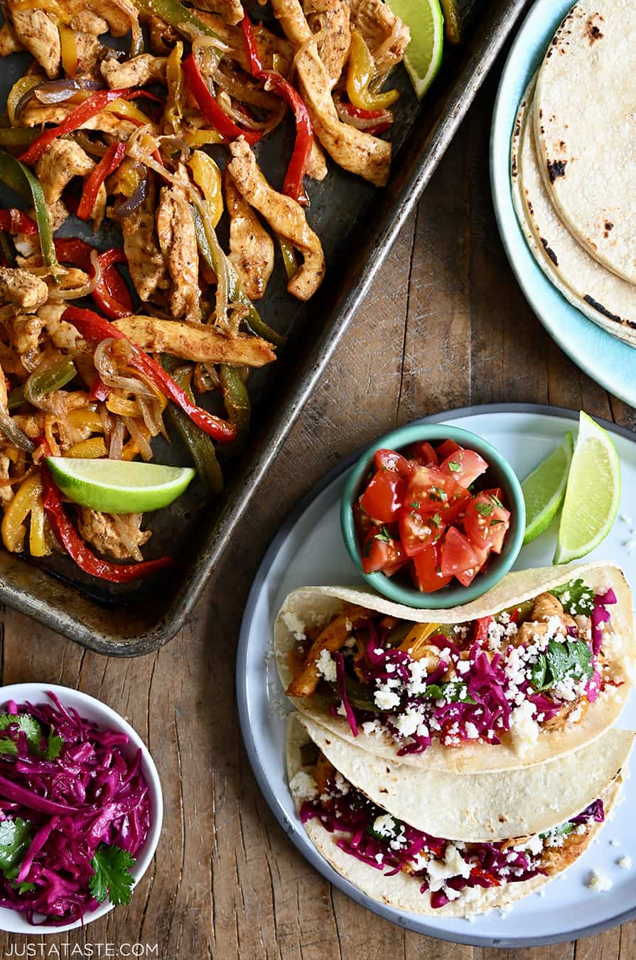 A top-down view of Sheet Pan Chicken Fajitas next to a plate with a stack of corn tortillas