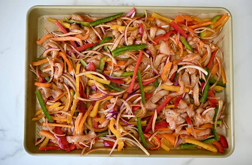 A baking sheet topped with uncooked chicken, bell peppers and red onions
