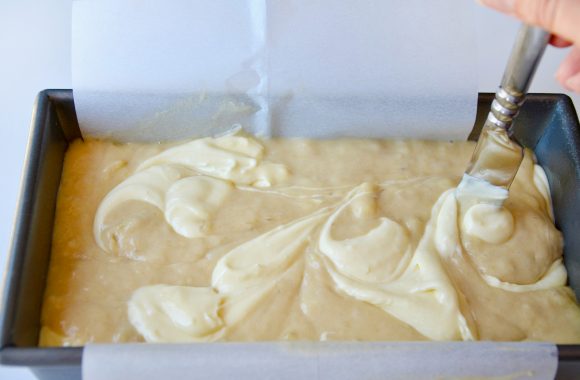 Knife swirling together banana bread batter and cream cheese mixture