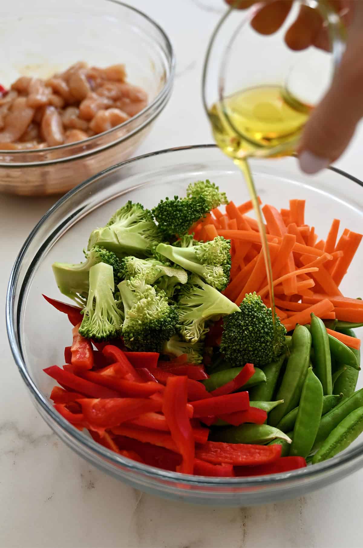 Pouring olive oil over veggies in a bowl.