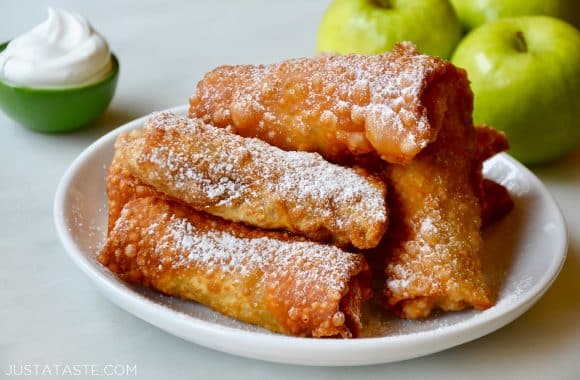 Apple pie egg rolls on a white plate dusted with powdered sugar