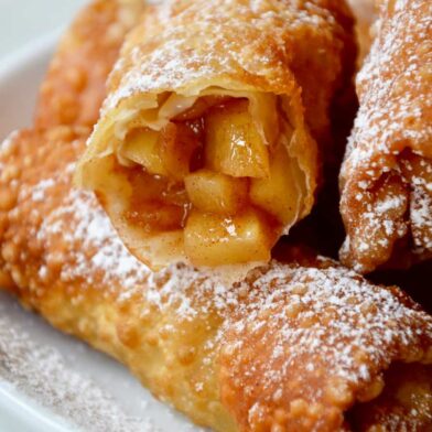 Apple pie egg rolls on a white plate with one cut open