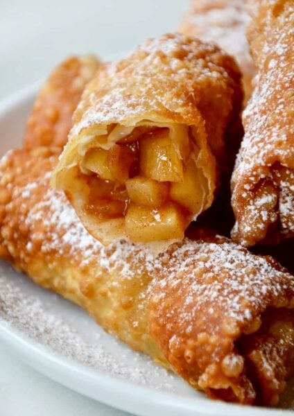 Apple pie egg rolls on a white plate with one cut open
