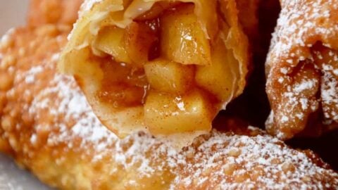 Apple pie egg rolls on a white plate with one cut open