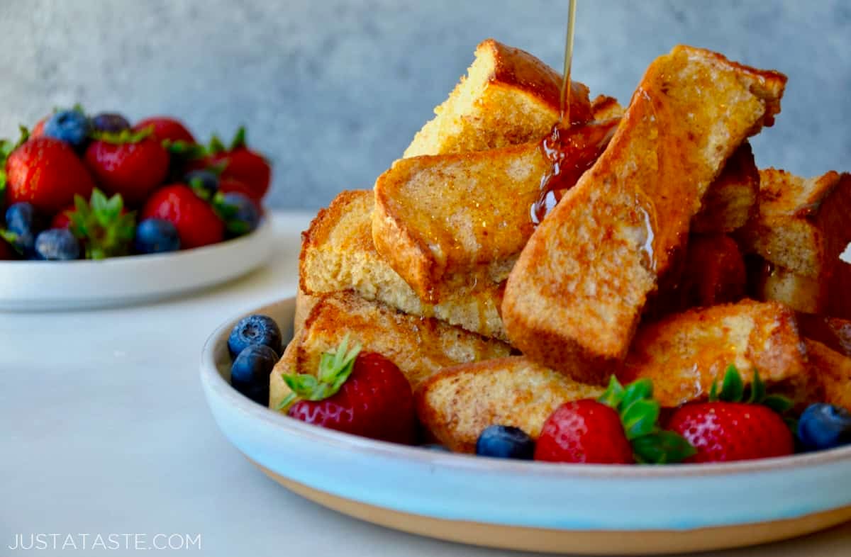 Baked French toast sticks drizzled with warm maple syrup on a plate with fresh berries.
