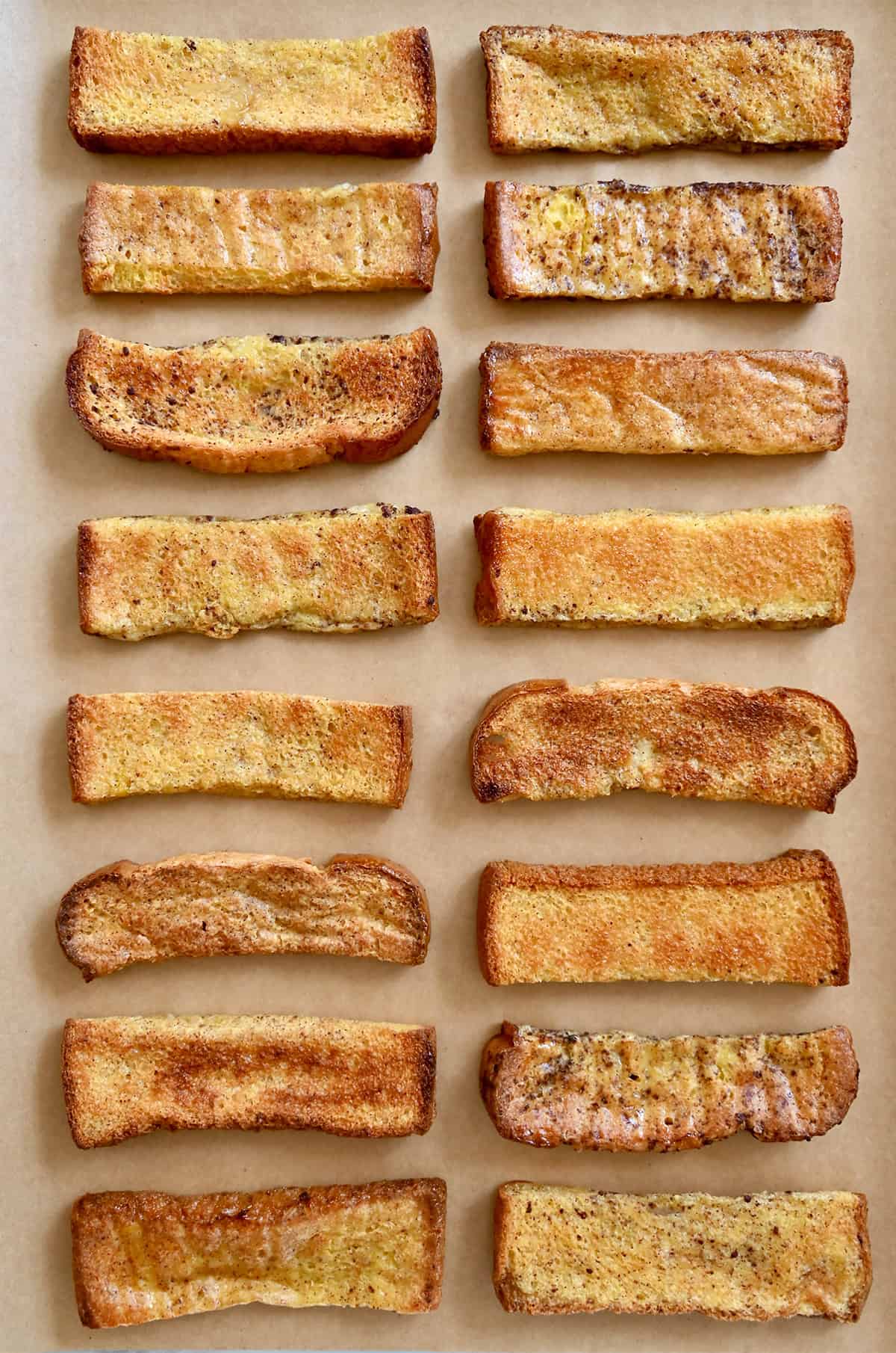Golden brown baked French toast sticks on a parchment paper-lined baking sheet.