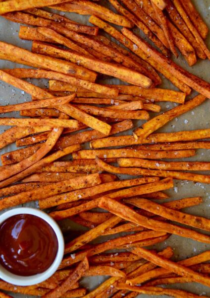 Baked sweet potato fries on a baking sheet with a bowl of ketchup