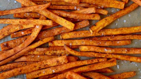 Baked sweet potato fries on a baking sheet with a bowl of ketchup