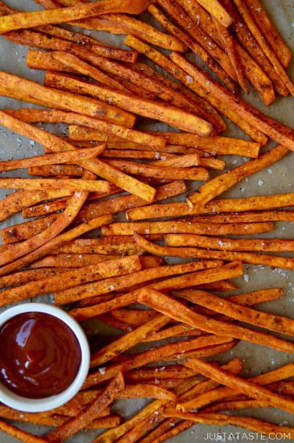 Baked sweet potato fries on a baking sheet with a bowl of ketchup
