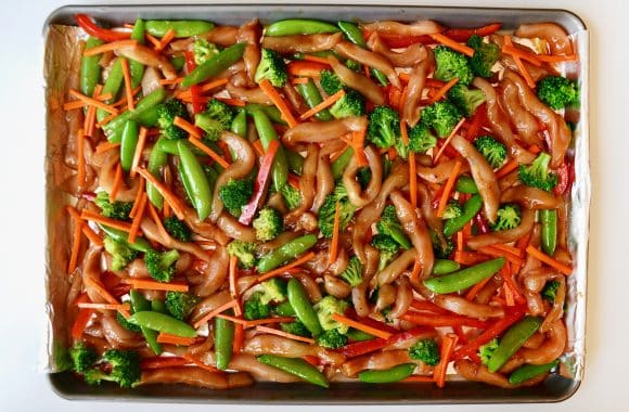 Raw chicken and vegetables arranged on a baking sheet