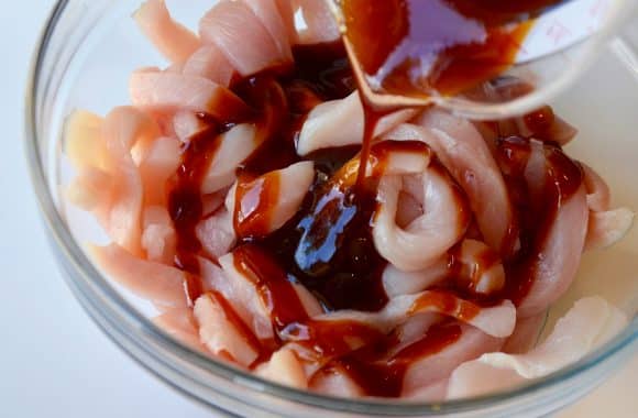 Raw sliced chicken in a glass bowl with teriyaki sauce on top