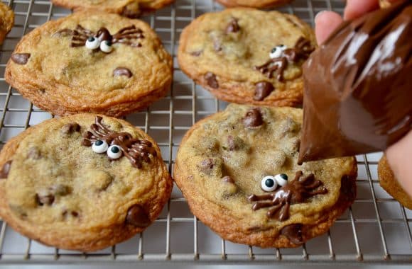 Piping chocolate spiders onto cookies