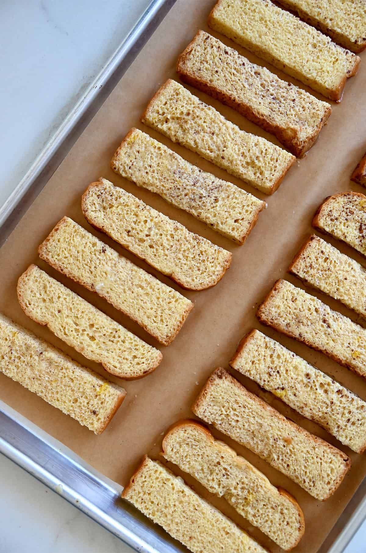 Custard-coated bread batons on a parchment paper-lined baking sheet before going into the oven to bake.