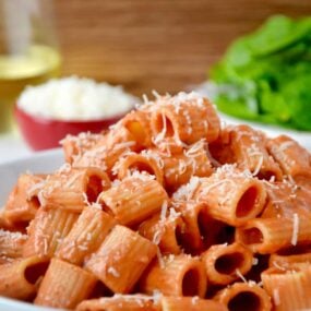 A white plate with vodka pasta on it and a salad in the background