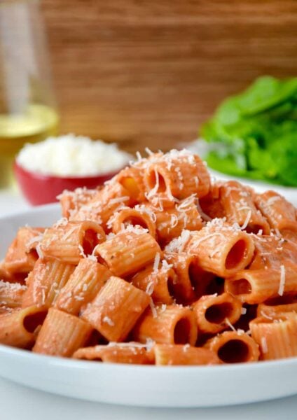 A white plate with vodka pasta on it and a salad in the background