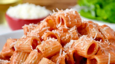 A white plate with vodka pasta on it and a salad in the background