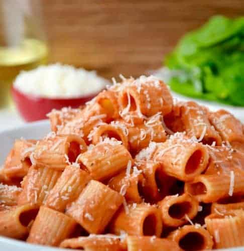A white plate with vodka pasta on it and a salad in the background