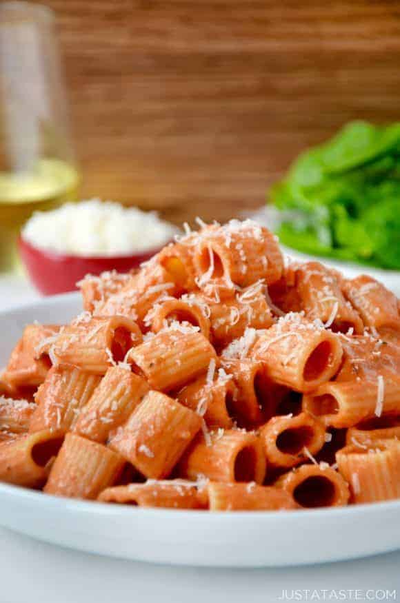 A white plate with vodka pasta on it and a salad in the background