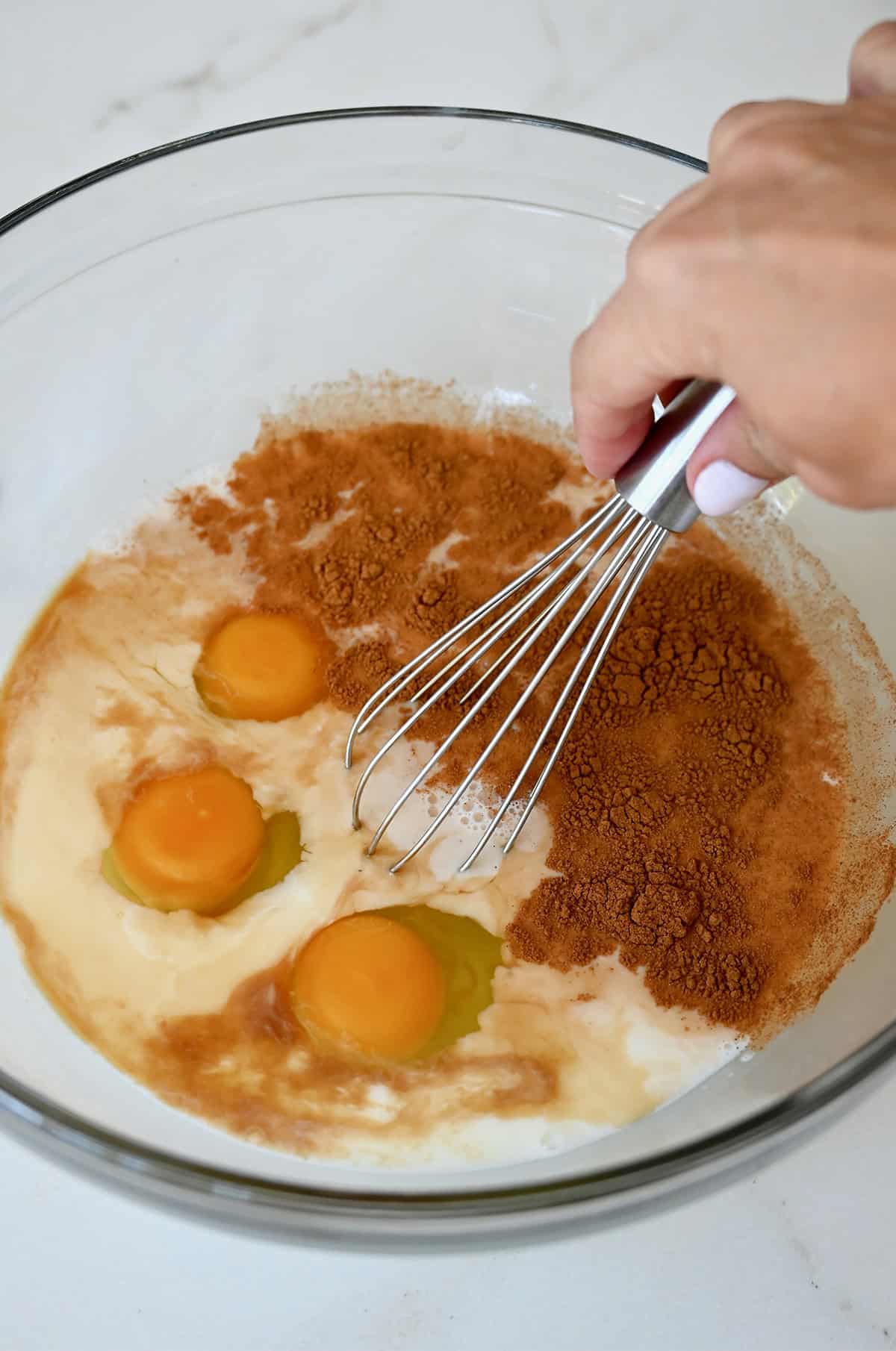 Whisking together eggs, milk, vanilla extract, and cinnamon to make a custard for French toast.