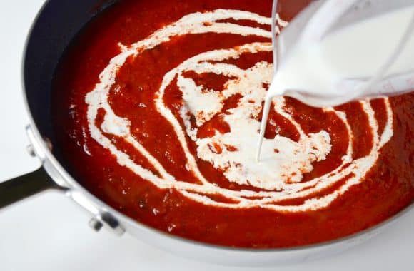 Tomato sauce in a pan with heavy cream being poured in