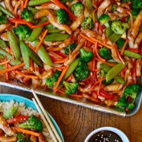 A sheet pan with chicken teriyaki and vegetable next to a plate