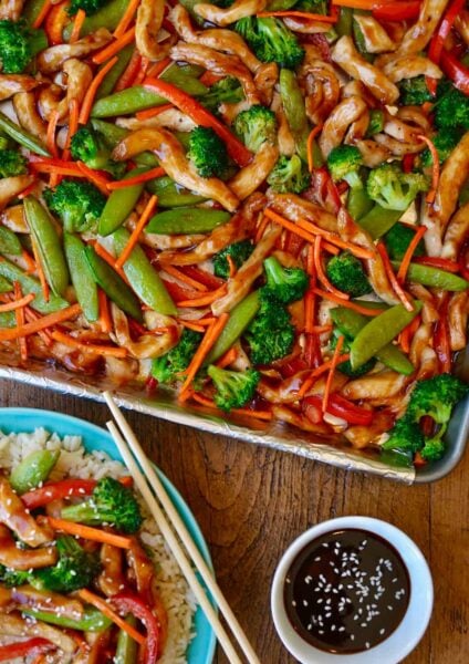 A sheet pan with chicken teriyaki and vegetable next to a plate