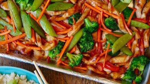 A sheet pan with chicken teriyaki and vegetable next to a plate