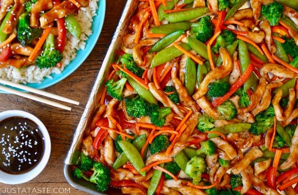 A sheet pan with chicken teriyaki and vegetables next to a plate with rice and chopsticks
