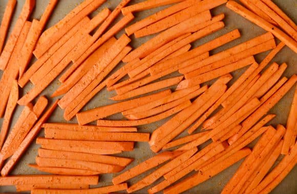 Uncooked sweet potato fries on a lined baking sheet