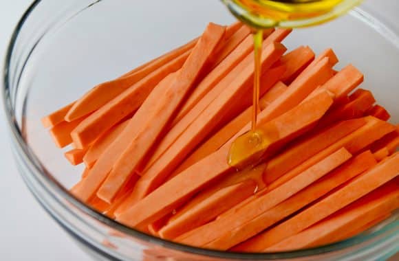 Cut sweet potato fries in a glass bowl with olive oil drizzled on top