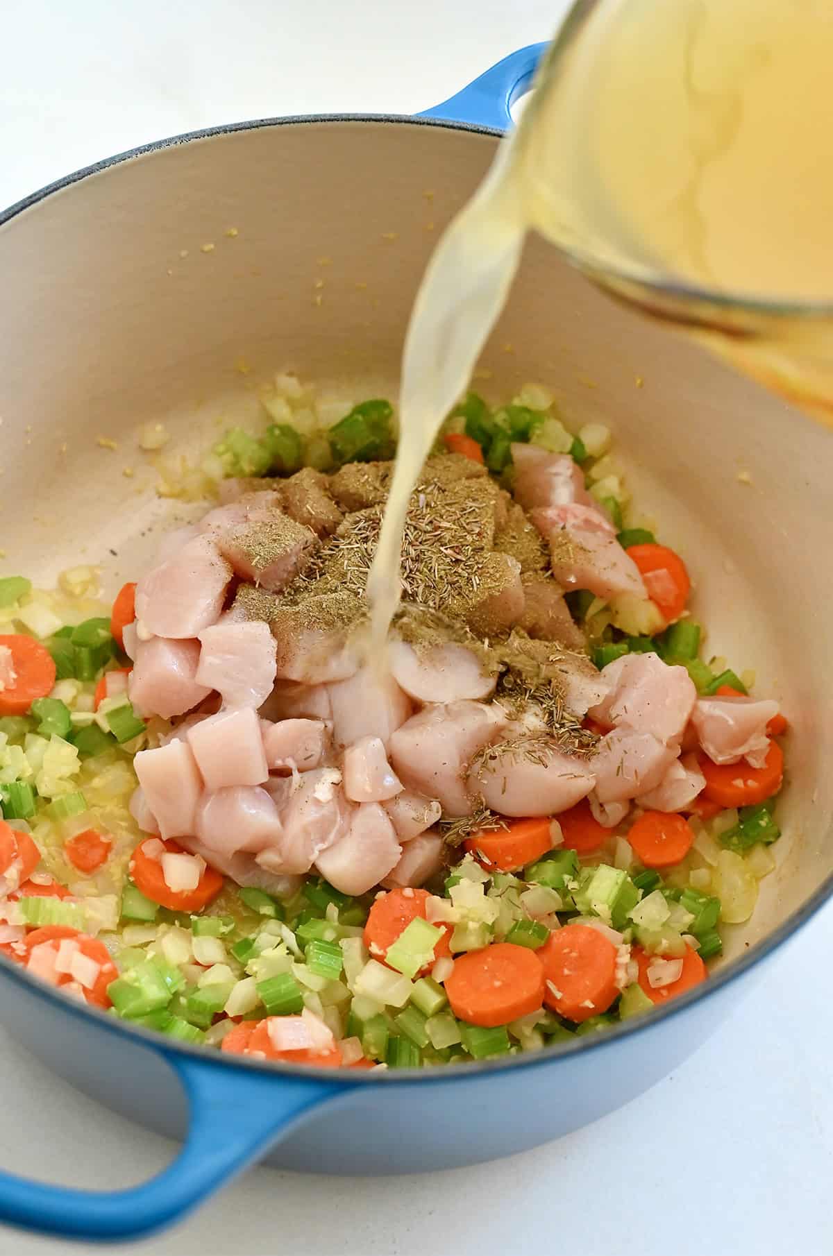 Adding chicken broth to a stockpot with sautéed veggies, spices and cubed chicken for soup.