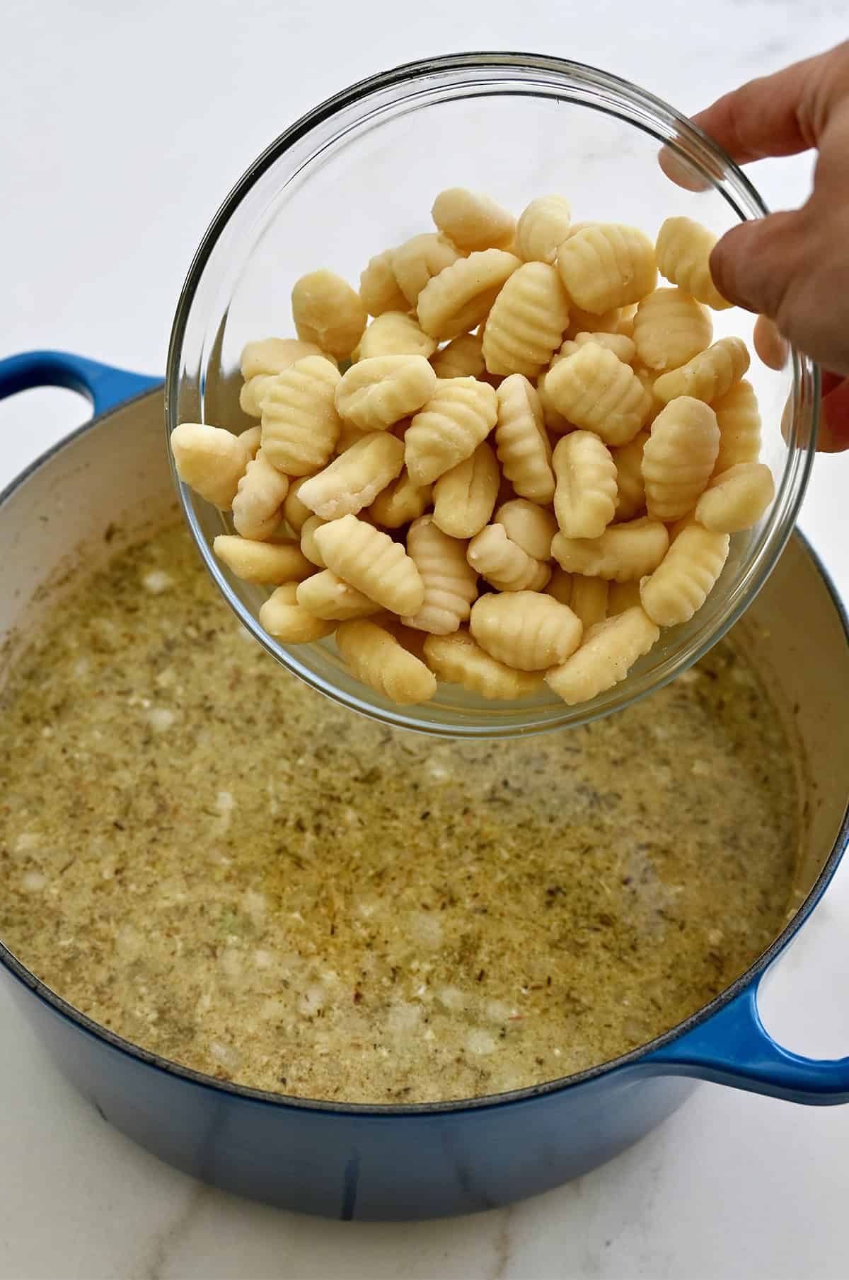 Adding potato gnocchi to a stockpot of chicken soup.