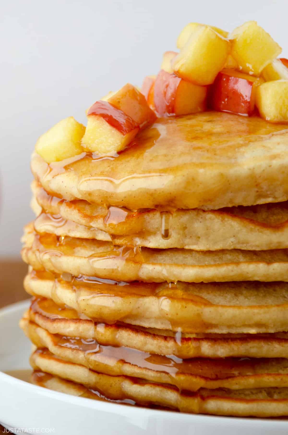 A tall stack of fluffy apple pancakes topped with caramelized sautéed apples and a drizzle of warm maple syrup.