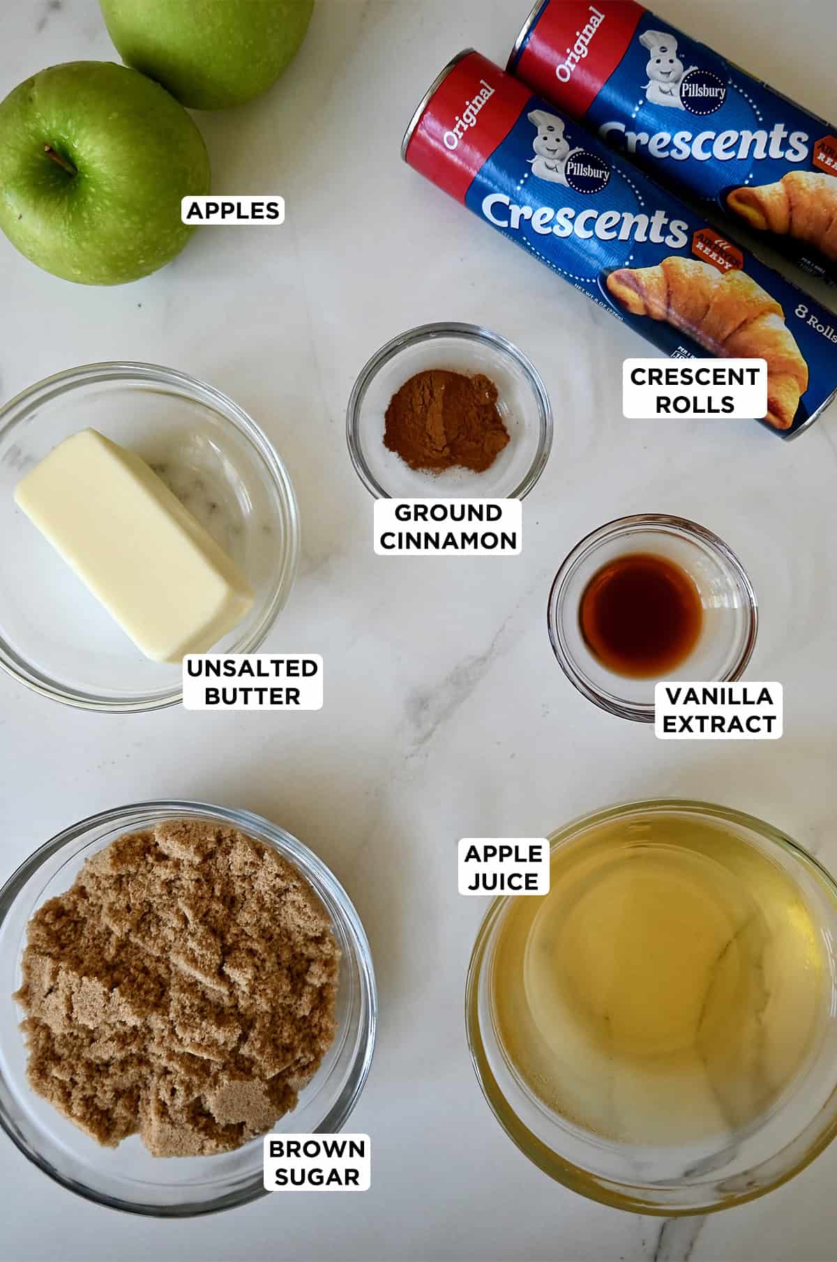 Ingredients to make apple dumplings with Pillsbury crescent rolls, including apples, butter, cinnamon, brown sugar, vanilla extract and apple juice.