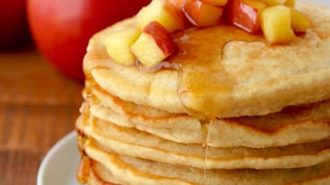 A tall stack of fluffy apple pancakes topped with sautéed apples and warm maple syrup.