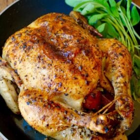 A skillet with a roast chicken stuffed with apples and sage