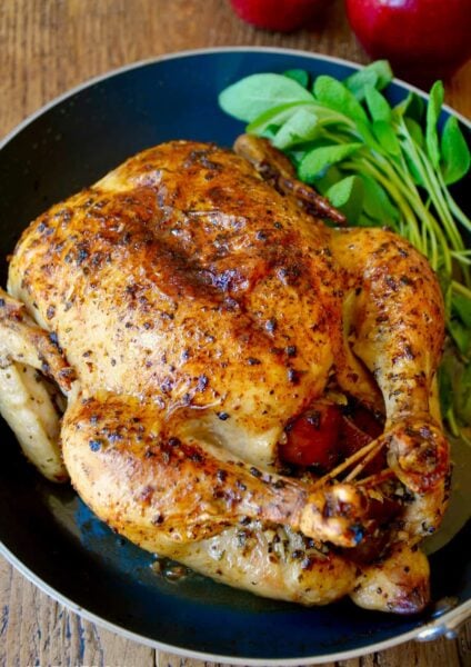 A skillet with a roast chicken stuffed with apples and sage