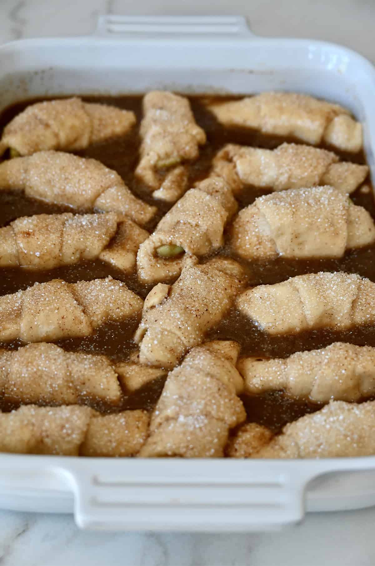 Crescent roll apple dumplings in caramel sauce before going into the oven to bake.