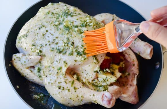 A raw chicken in a skillet being brushed with garlic butter