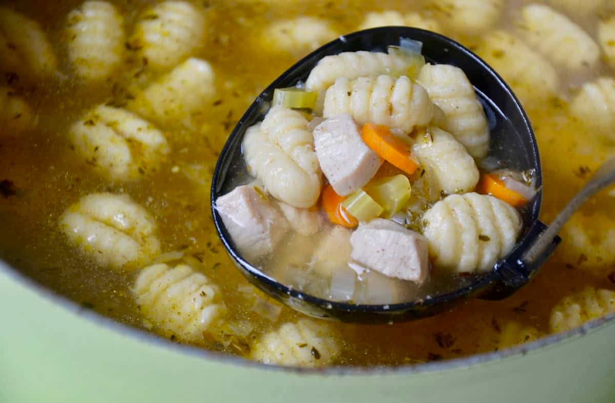 A ladle scoops chicken gnocchi soup out of a large stockpot.