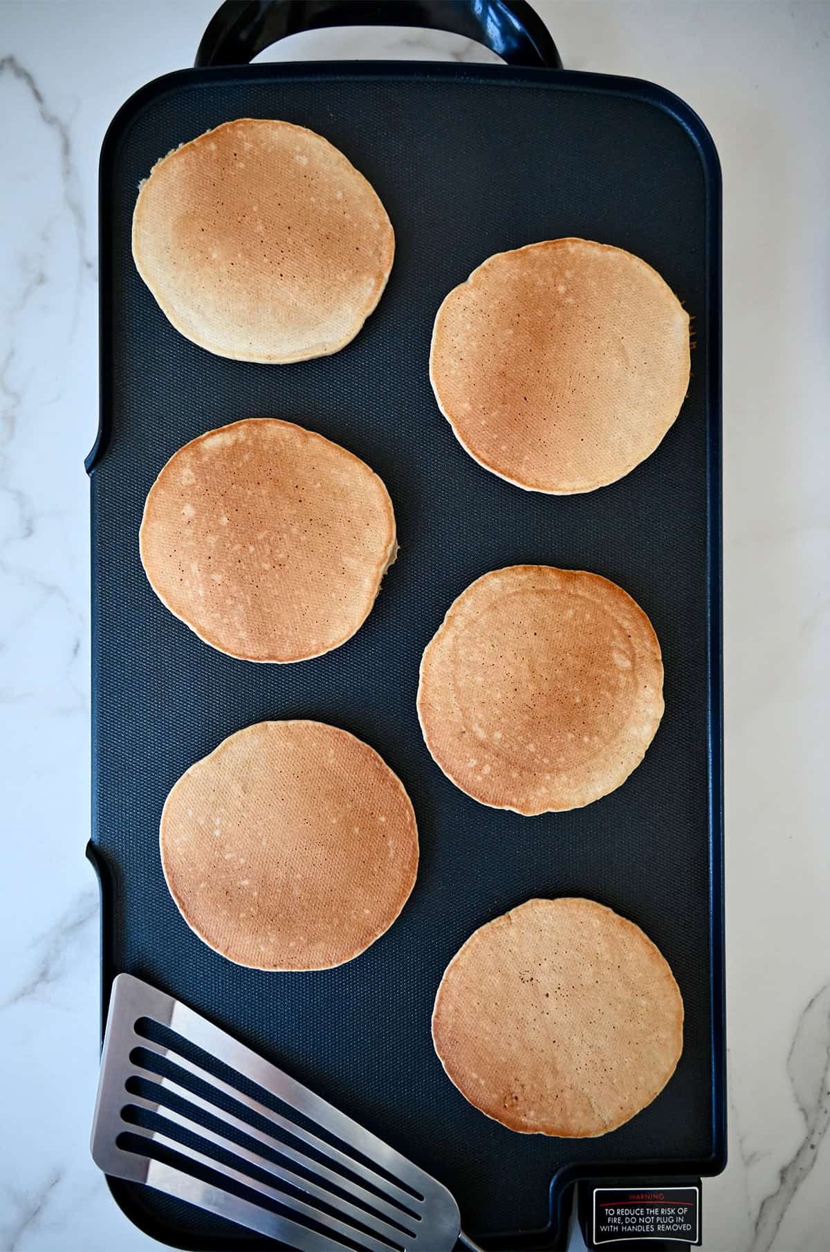 Golden brown apple cinnamon pancakes on a griddle next to a fish spatula.